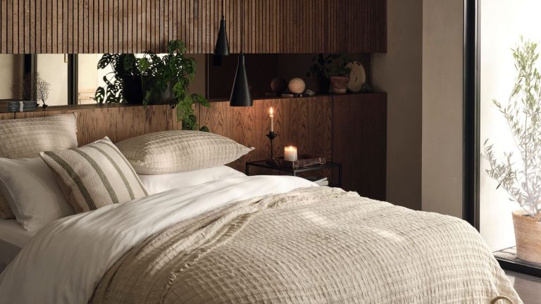 Un « investissement dans votre sommeil et votre santé mentale » : cette alarme de lever du soleil peut à elle seule vous aider à vous lever les matins d’hiver et à éviter la paresse A warm rustic bedroom with wooden headboard stretching aling a whole wall, and a large bed with neutral bedding