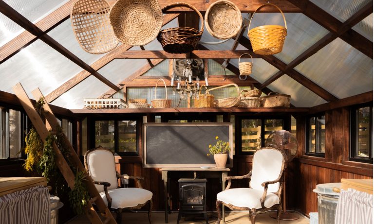 Le hangar d’empotage : si vous souhaitez obtenir de l’aide pour équilibrer un espace de jardin fonctionnel avec un charme nostalgique, cette serre du Tennessee répond à toutes les attentes Greenhouse styled with antique chairs, a wood burning stove and wicker harvest baskets hanging from ceiling beam