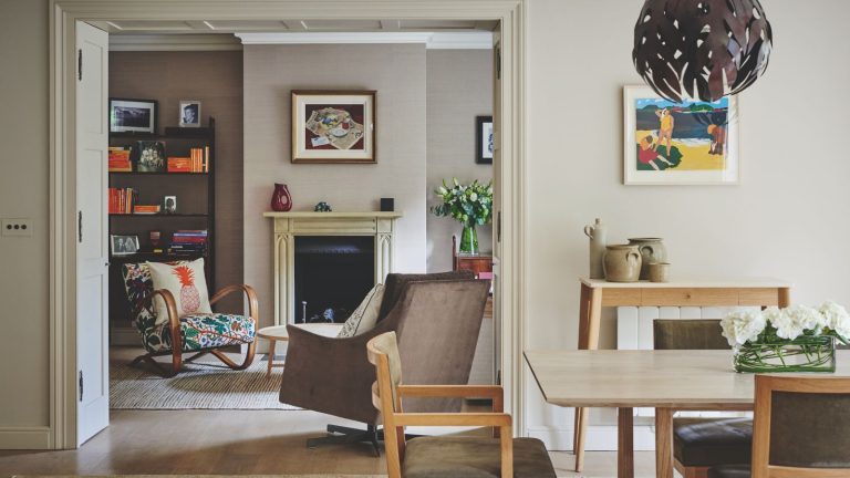 La « différence entre la vie et la mort » : des experts en entretien ménager révèlent 3 tests de détecteur de fumée que vous devez effectuer en octobre A neutral dining area with wooden chairs and table, and a doorway through to an eclectic neutral living room with upholstered chairs, a black fireplace with cream mantelpiece, artwork, flowers, and a black shelving unit filled with books.