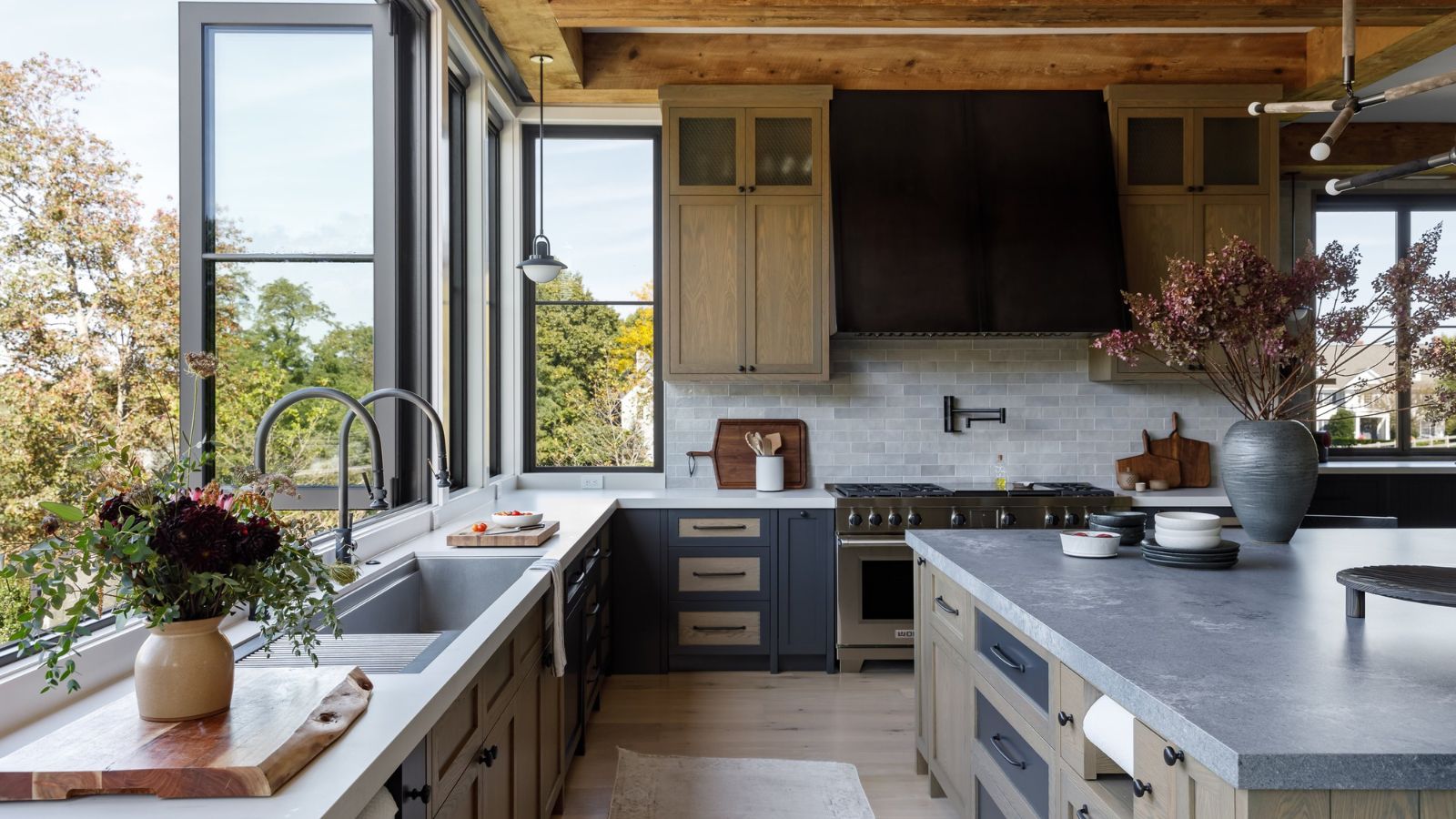 Grande cuisine avec fenêtres pliantes et îlot. Il est lumineux, ouvert et dispose de fenêtres à triple aspect montrant l'élévation de la maison avec des arbres tout autour.