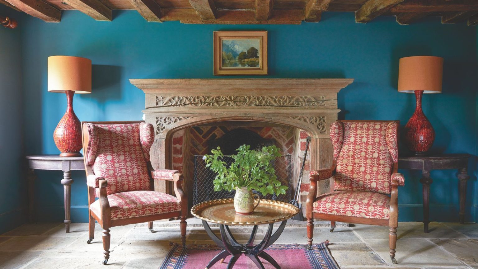 Votre foyer est une bombe à retardement, prévenez les professionnels du CVC – Cette astuce d’entretien à 10 $ augmentera la sécurité tout l’hiver Colorful sitting room with two red patterned armchairs, an ornate fireplace, a side table with potted plant, a red rug, pictured in front of bright blue wall with wooden-beamed ceiling above.