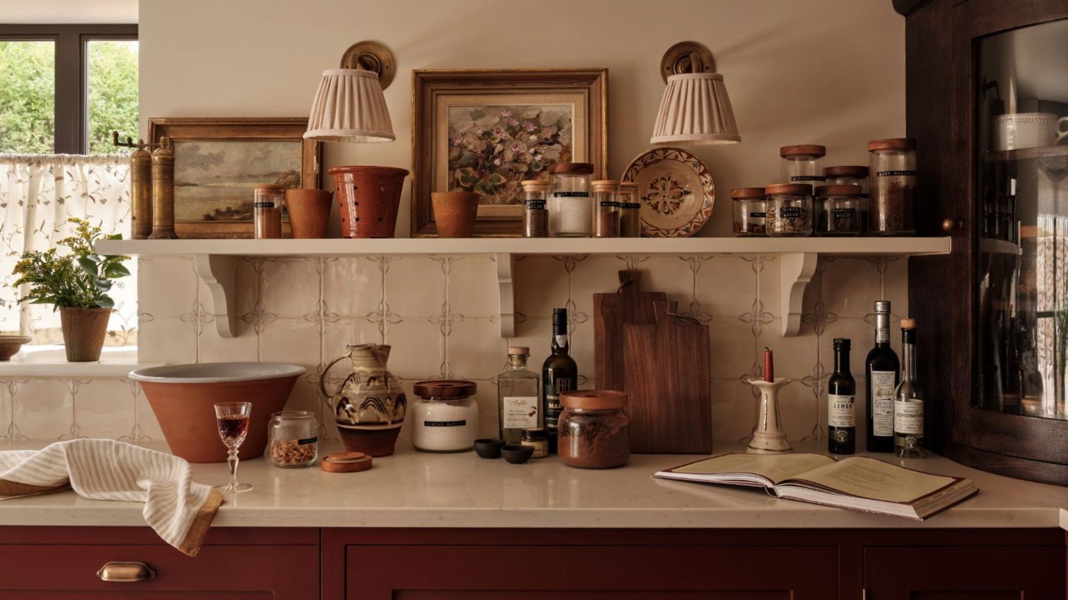 Ma méthode de zonage simple évite la contamination dans ma cuisine – c’est le secret de sécurité alimentaire que je jure par dans un foyer souffrant de TOC. A kitchen with red cabinets, white worktops and white tile backsplash. Close up of the counter and a wall-mounted shelf covered in cozy kitchen clutter.