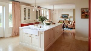 A soft kitchen with warm white cabinets, red and white striped curtains, and a cozy seating area with a patterned sofa and armchair