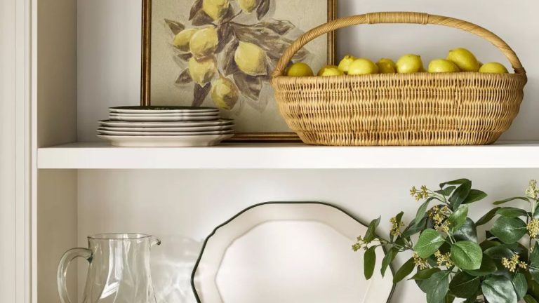 Fatigué de la vaisselle sale ? J’ai commencé à mettre des citrons dans mon lave-vaisselle – voici pourquoi je ne le chargerai plus jamais sans eux kitchen shelves with a woven basket filled with lemons and a vintage-style lemon painting with stacked crockery