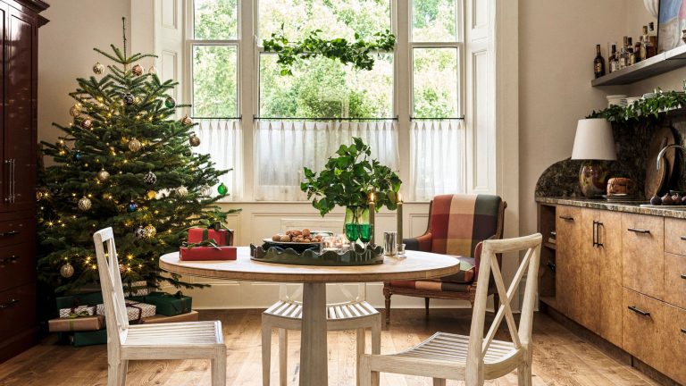 Open plan kitchen decorated for Christmas with a christmas tree in one corner and a burl wood kitchen and circular dining table in the center