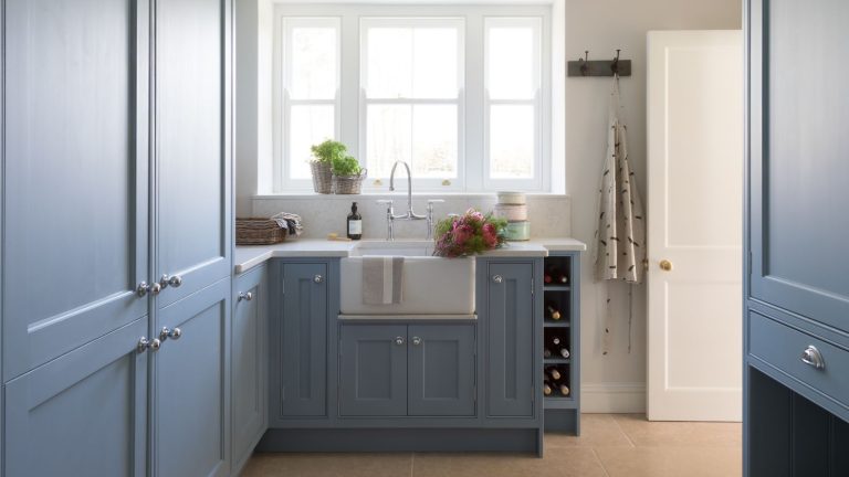 C’est le seul héros de lessive à 9 $ dont vous avez besoin pour empêcher la literie d’hiver de s’accumuler dans la sécheuse – cela réduira même également votre facture d’énergie. A utility room with blue built-in cabinets and a white farmhouse sink beneath a large framed window.