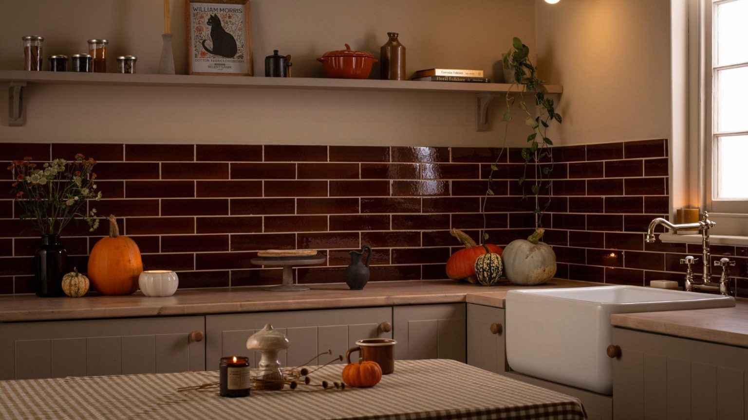 Je suis obsédée par l’automne et j’écris sur le nettoyage pour gagner ma vie. Voici mes meilleurs produits de nettoyage sur le thème de l’automne pour un rafraîchissement saisonnier parfaitement confortable. A dimly lit kitchen with deep red subway tile backsplash. Various sized pumpkins scattered on the counters.