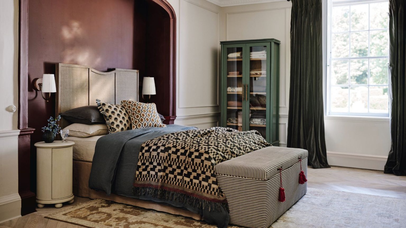 Ce sont les 7 choses que je remarque toujours dans les chambres en désordre en tant qu’organisateur professionnel – voici comment les nettoyer pour de bon A wooden bed set into a red-painted alcove in a large bedroom. Patterned bedding on the bed and a grey pin-stripe ottoman at the foot.