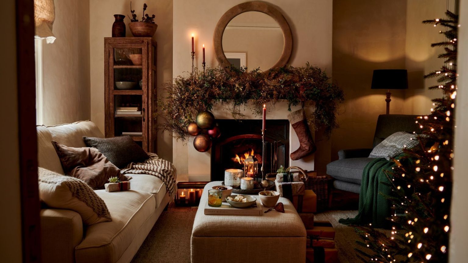 Les organisateurs professionnels révèlent comment réduire de moitié la décoration de Noël maintenant vous fera gagner du temps et réduira le stress l’année prochaine A warm Christmas living room, with lime washed walls and a fireplace. A large wreath over the mantel with a hanging stocking. The edge of a tree visible from the edge of the doorway.