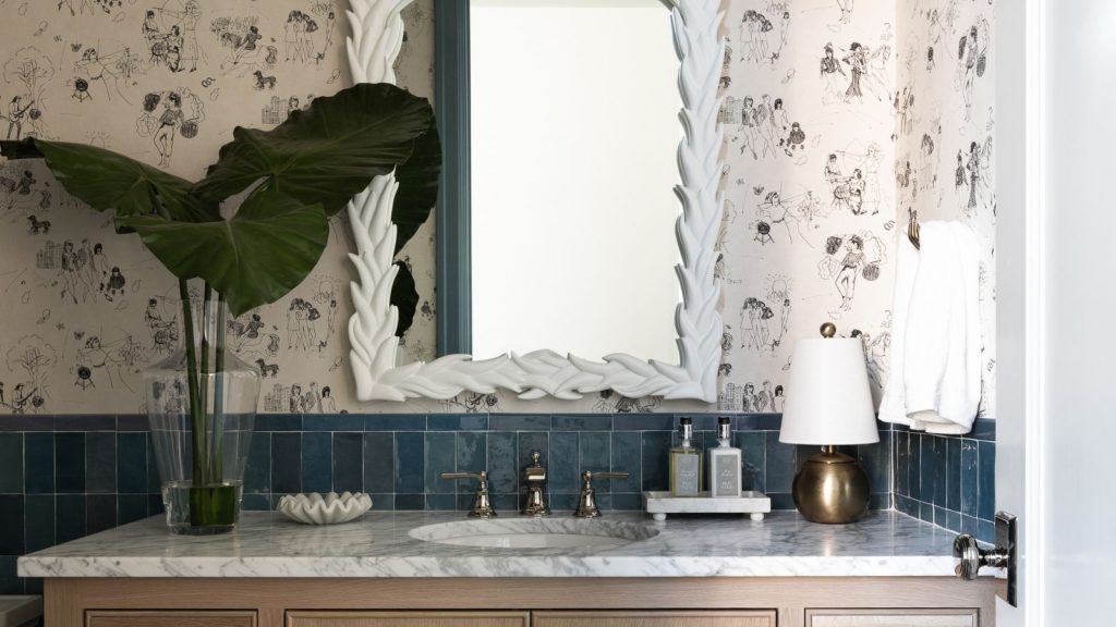 A close-up of a wooden bathroom vanity with a marble countertop decorated with a vase of leaves and a gold lam
