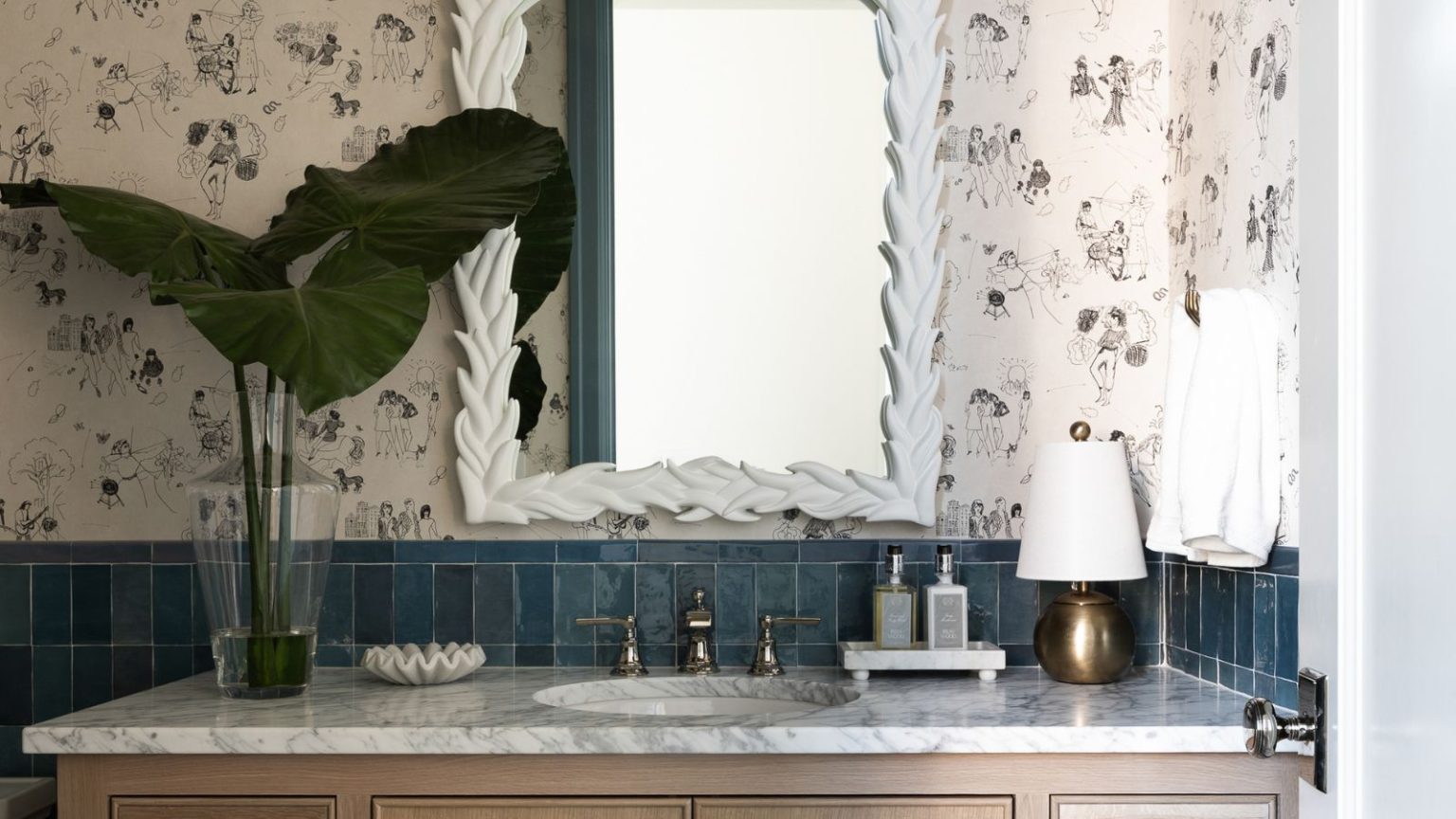 La seule chose qui manque à votre salle de bain cet hiver – les designers disent que c’est la réponse simple à un espace plus confortable, plus chaleureux et plus accueillant A close-up of a wooden bathroom vanity with a marble countertop decorated with a vase of leaves and a gold lam