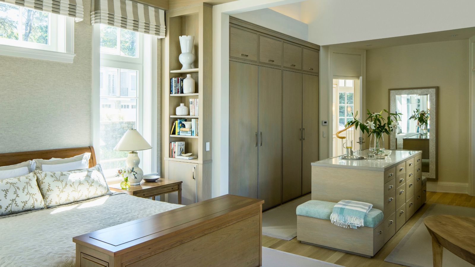 Grande chambre neutre à gauche avec dressing à droite. Le placard a des placards encastrés visibles du sol au plafond, ainsi qu'un îlot avec tiroirs de rangement. Le décor naturel est apaisant et neutre, avec des rayures et des accents bleus
