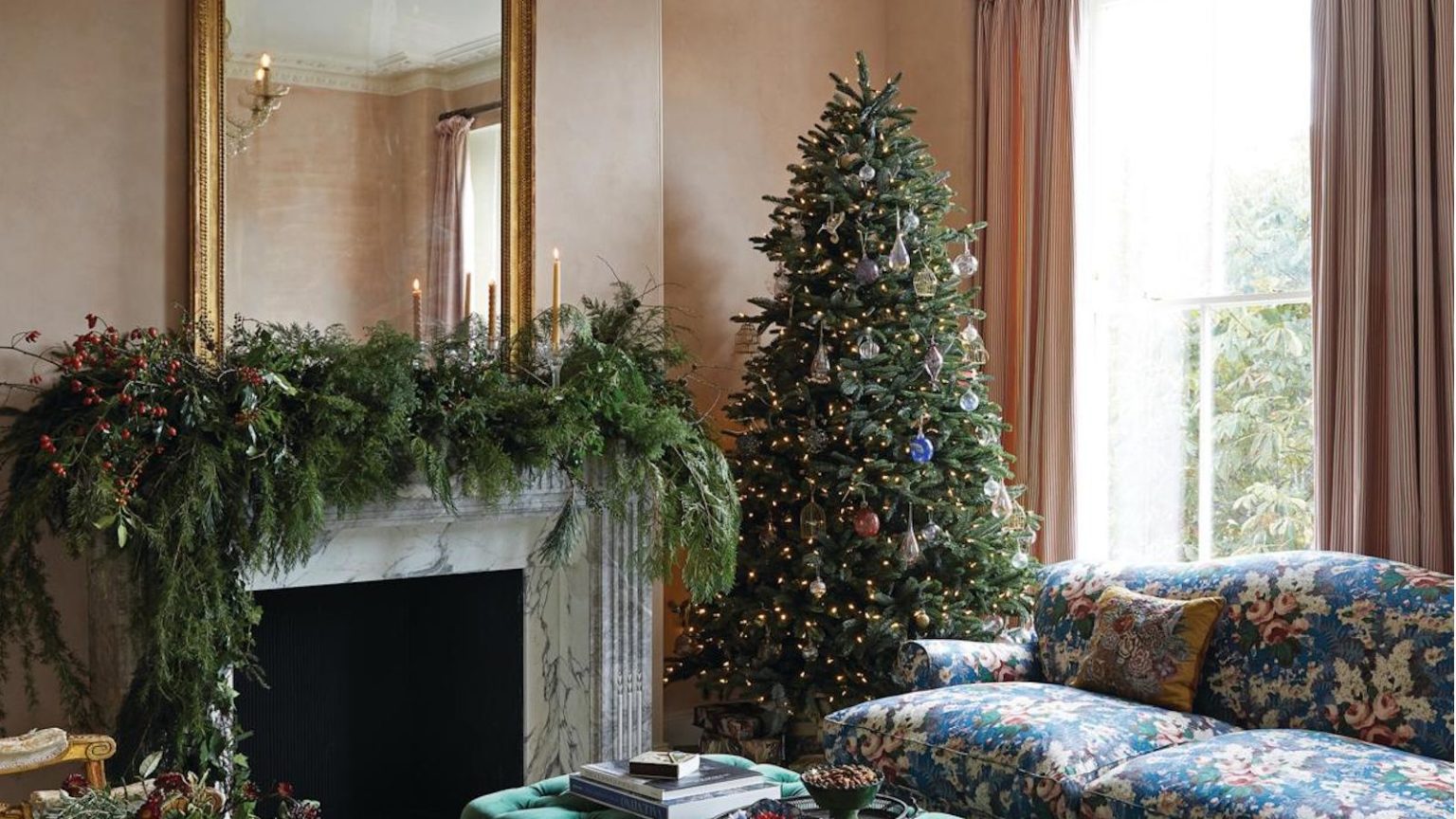 Avant d’accrocher une seule décoration d’arbre de Noël, lisez ceci : un expert prévient qu’il y a une étape cruciale que vous sautez probablement Christmas tree in living room next to blue floral couch. Garland on the mantelpiece