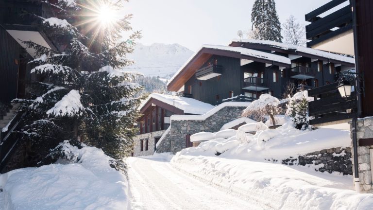 A large luxury home up a steeped driveway, covered in snow. Mountains in the background.