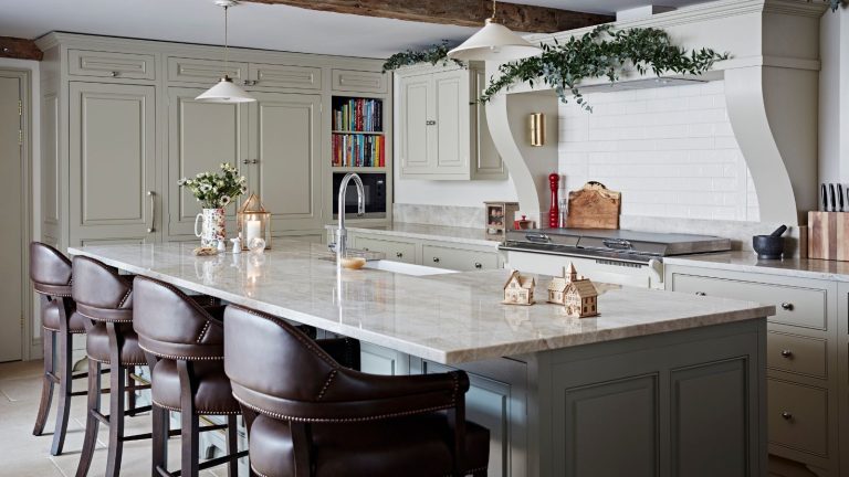 A festively decorated kitchen with white cabinets, white backsplash and range hood, and a large kitchen island with white marble countertop and four leather barstools.