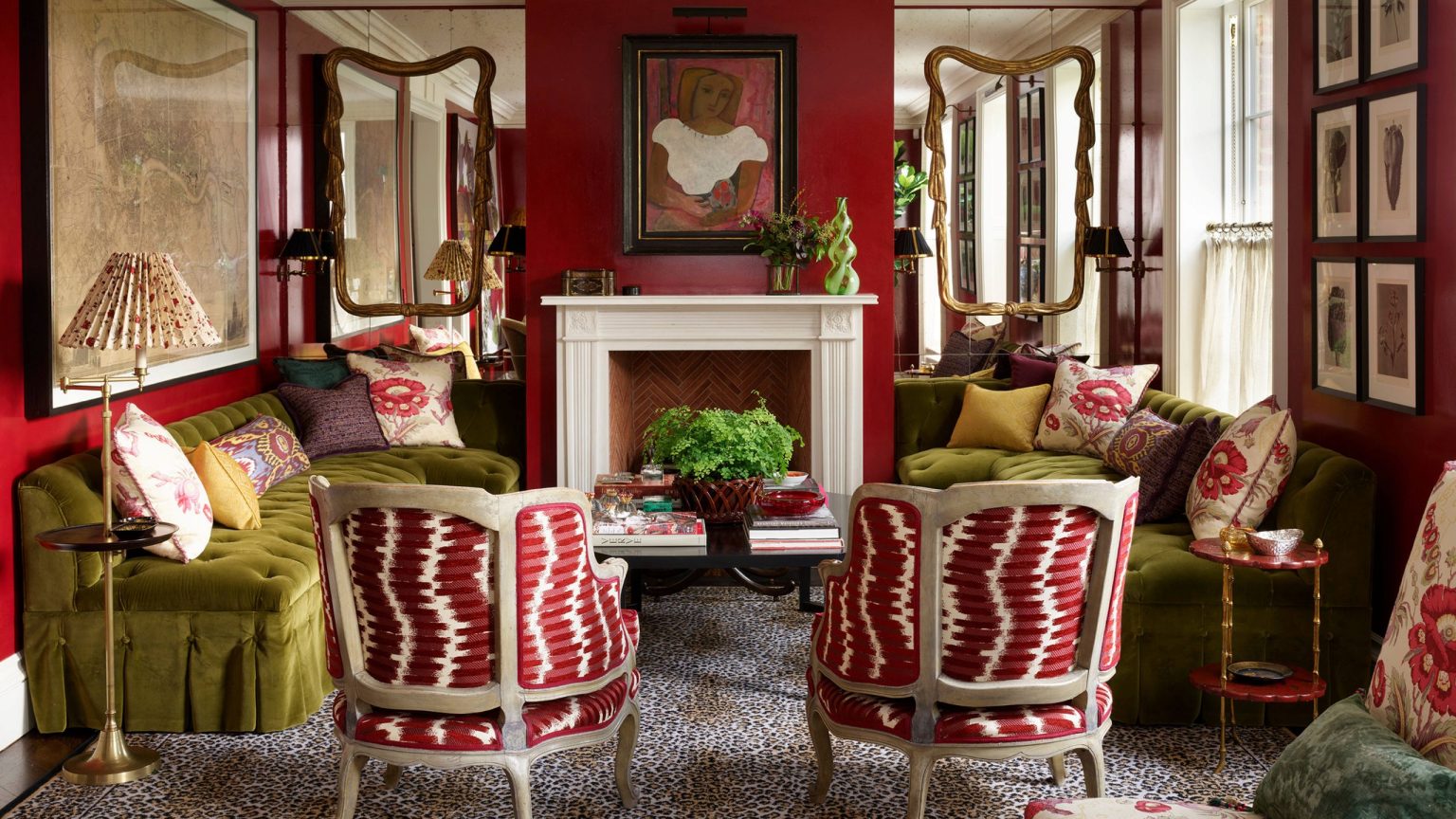 Faites le tour d’une maison familiale luxueusement superposée qui se glisse si facilement en mode fête de Noël Bold living room featuring deep red walls, two olive green velvet sofas facing a fireplace, and two armchairs with red and white patterned fabric on a leopard print rug