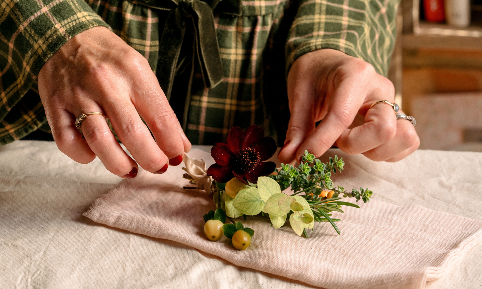 Pétales et racines : ne vous inquiétez pas si vous n’avez pas de place sur votre table à manger des fêtes pour les fleurs – je vous ai couvert avec ma charmante idée de bouquets de serviettes Hands arranging flowers and foliage on a pink cotton napkin