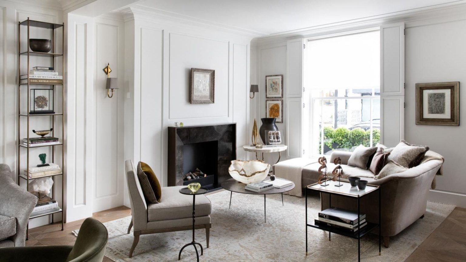 Feng Shui Pro révèle l’habitude facile à prendre à la maison avant le 1er janvier pour éliminer les obstacles et laisser couler le bonheur et le succès en 2026 A white living room with neutral furniture, large windows, white panelled walls, a patterned pale Persian-style rug, and a black marble fireplace in the center of the back wall. To the left of the fireplace is a tall shelving unit with books and decorations.