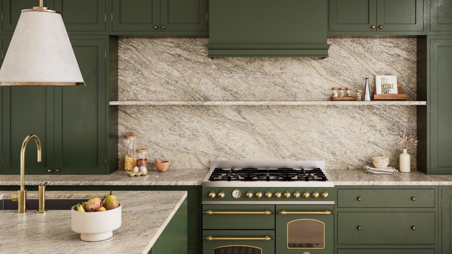 Modern, cohesive green kitchen with marble countertops, and floating shelves surrounded by green cabinets. A bowl of fruit is pictured on a kitchen island in the foreground, below a white lampshade.