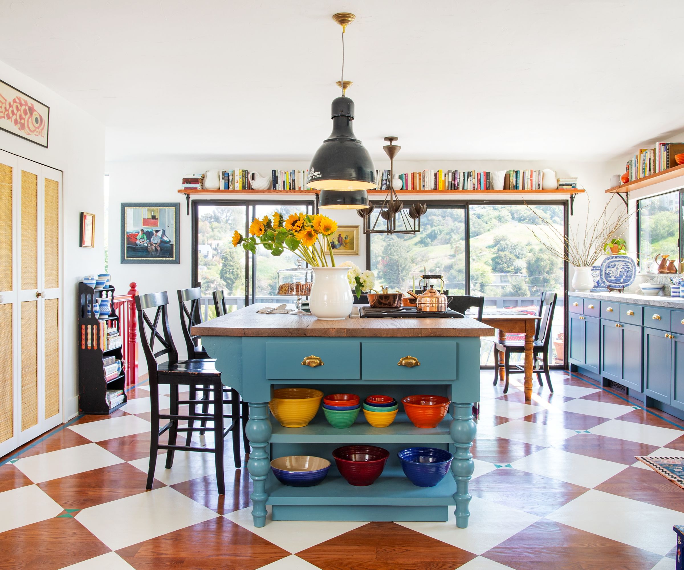 Une cuisine colorée avec des murs blancs, des armoires bleues et du parquet peint avec un motif en damier