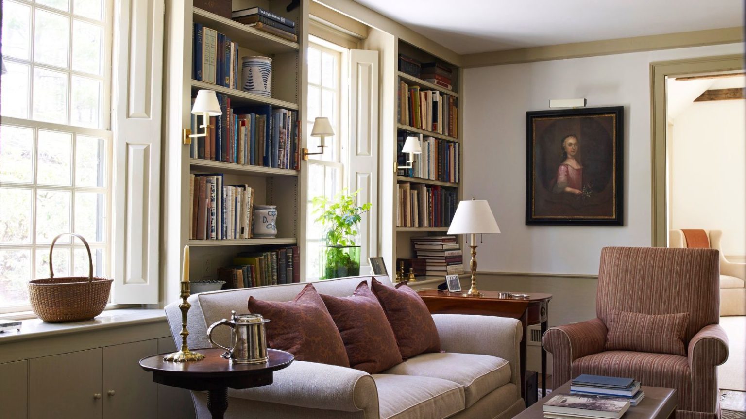 6 erreurs d’entreposage hivernal que tout le monde commet – Les organisateurs professionnels révèlent des solutions pour éviter les odeurs de moisi, les dommages causés par les parasites et les nuisances oculaires inutiles A cozy living room with build in book shelves between windows. A cream sofa in front beside a brown upholstered arm chair.