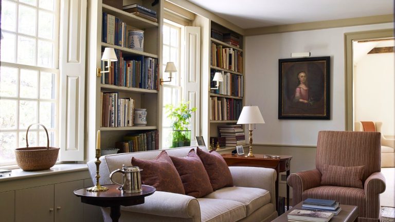 6 erreurs d’entreposage hivernal que tout le monde commet – Les organisateurs professionnels révèlent des solutions pour éviter les odeurs de moisi, les dommages causés par les parasites et les nuisances oculaires inutiles A cozy living room with build in book shelves between windows. A cream sofa in front beside a brown upholstered arm chair.