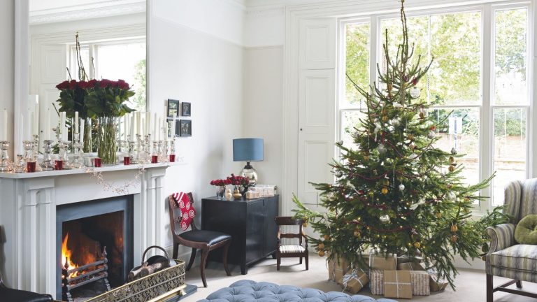 Arrêtez d’acheter des bacs de rangement en plastique lorsque ces 5 articles ménagers réutilisables que vous possédez déjà feront le travail gratuitement Festive living room with large Christmas tree, padded blue ottoman, white fireplace and mantelpiece with large mirror, white walls and large windows with white shutters.