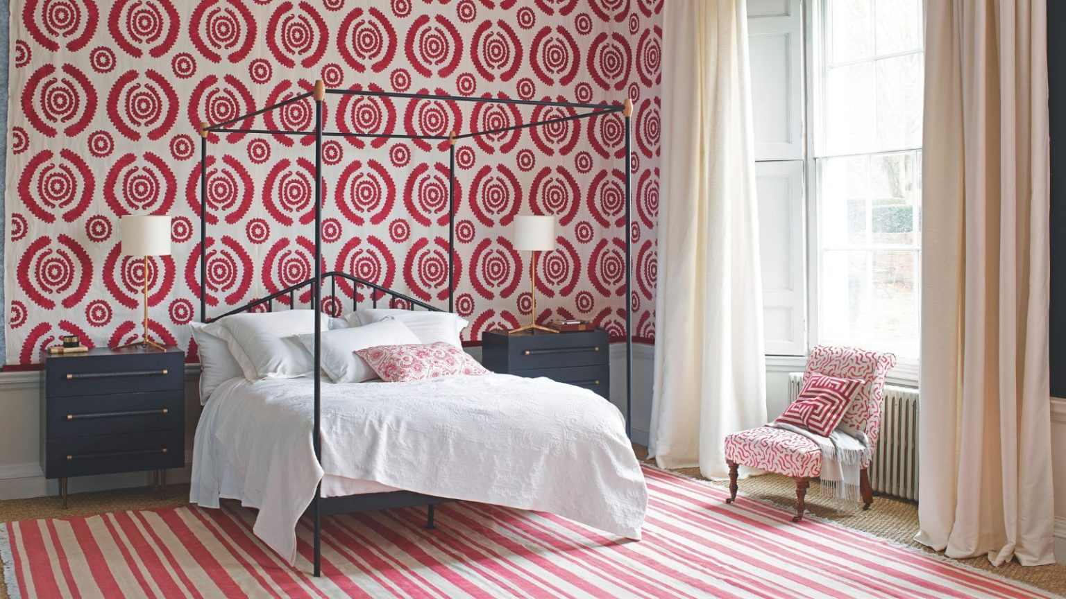Marre des nuits froides ? Les professionnels du CVC révèlent une modification rapide et gratuite de la chambre à coucher pour vous garder au chaud sans augmenter les factures A red and white bedroom with patterned wallpaper and rug, and large black four poster bed with white bedding, black bedside tables, a white and red upholstered chair, and white curtains over a large window.