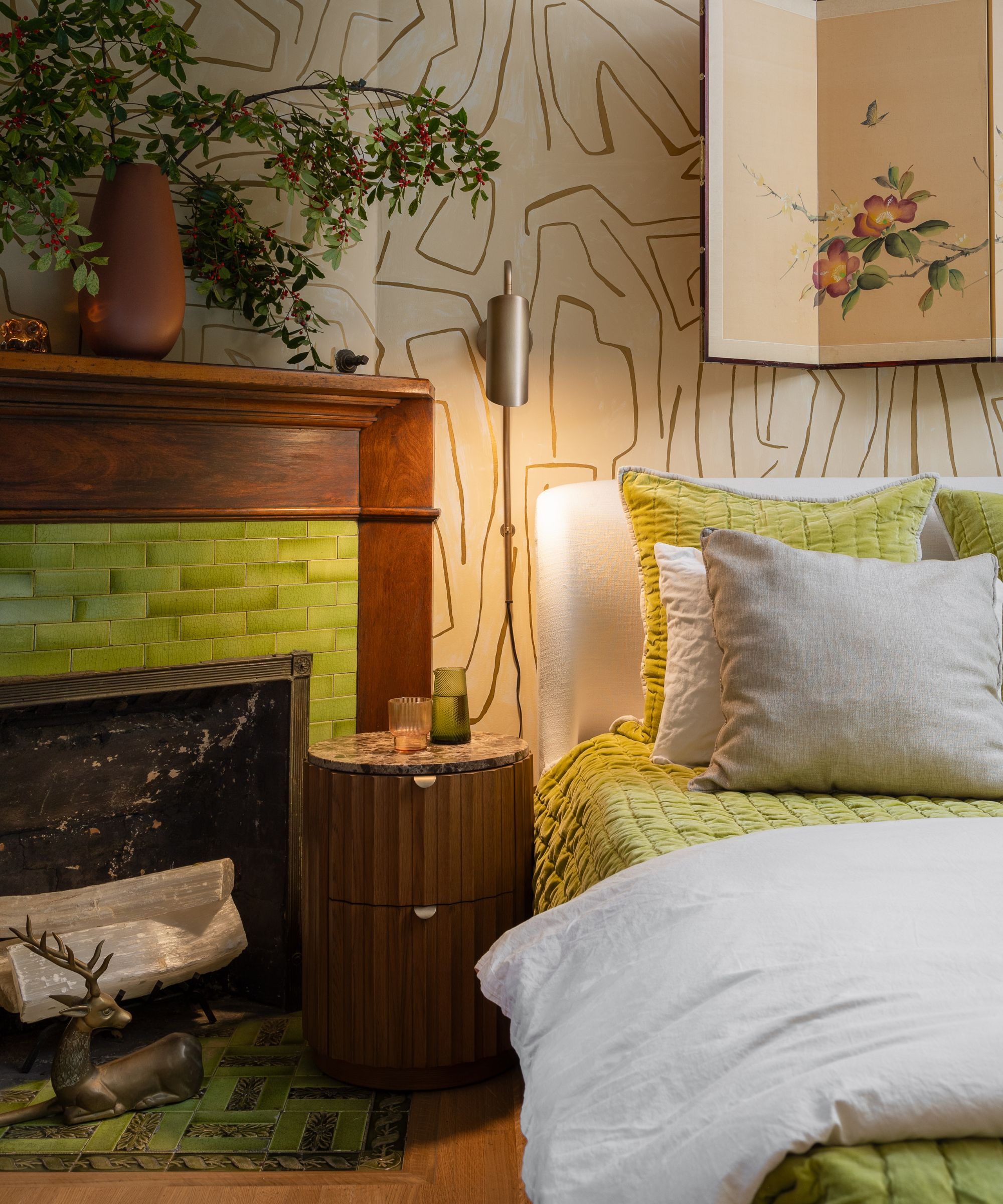 Coin chambre avec un lit blanc et vert anis, une table de nuit ronde en bois et une cheminée avec un contour carrelé vert vif