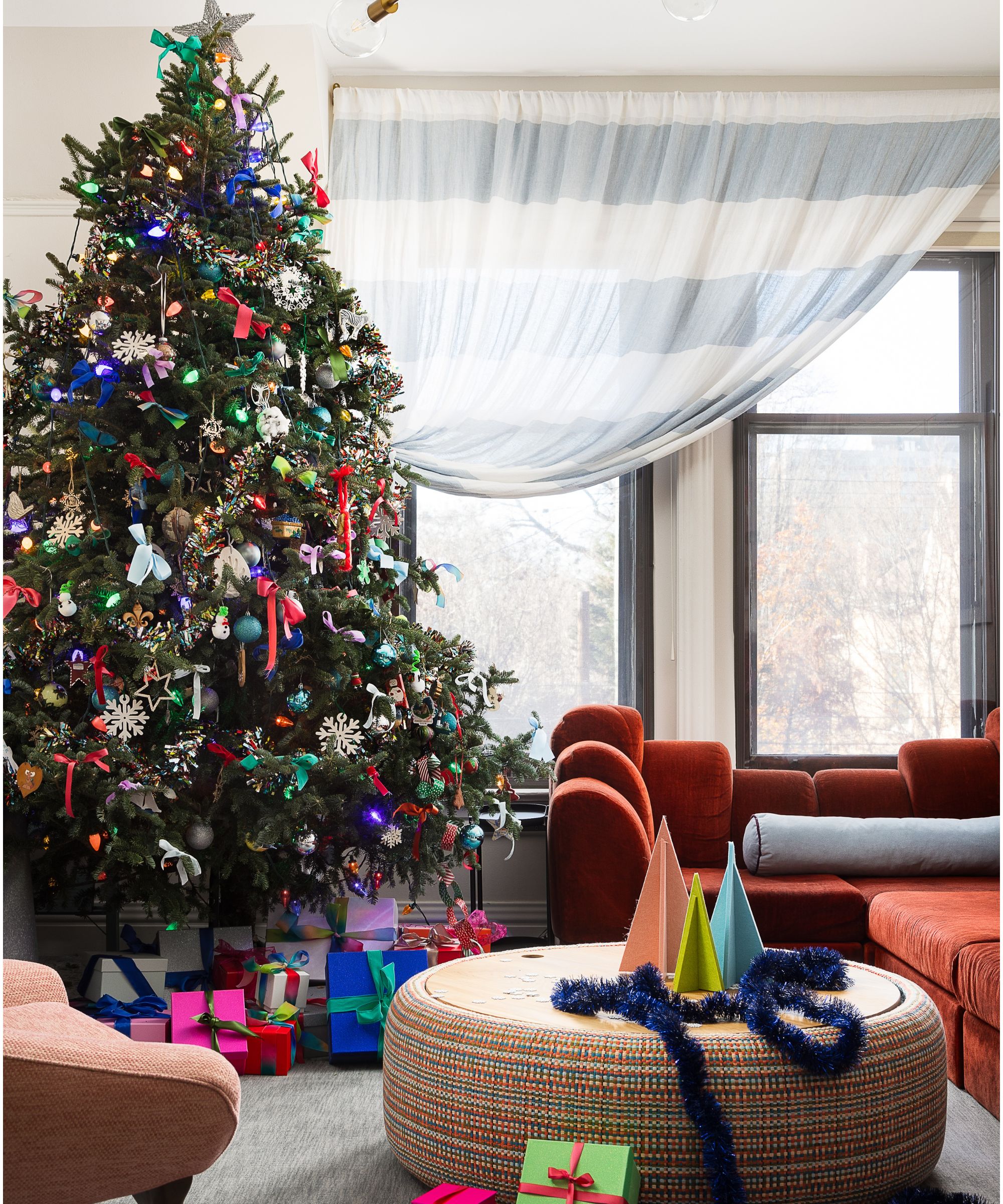 la créatrice Bethany Adams' salon décoré pour Noël avec un canapé en velours rouille, un pouf décoré d'arbres en papier et un grand sapin de Noël coloré