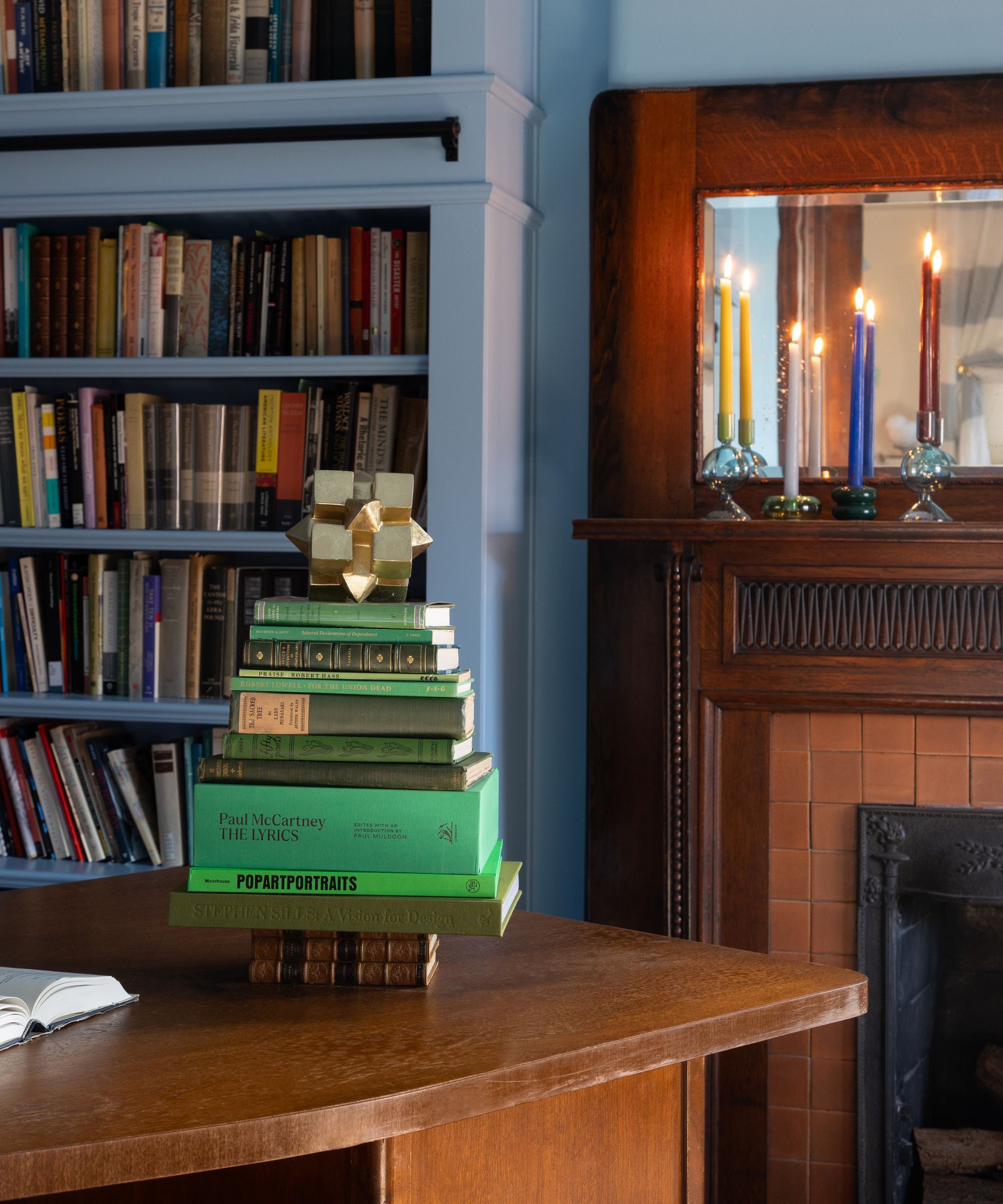 salon peint en bleu avec une cheminée historique en bois foncé décoré pour Noël avec une pile de livres verts en forme d'arbre de Noël