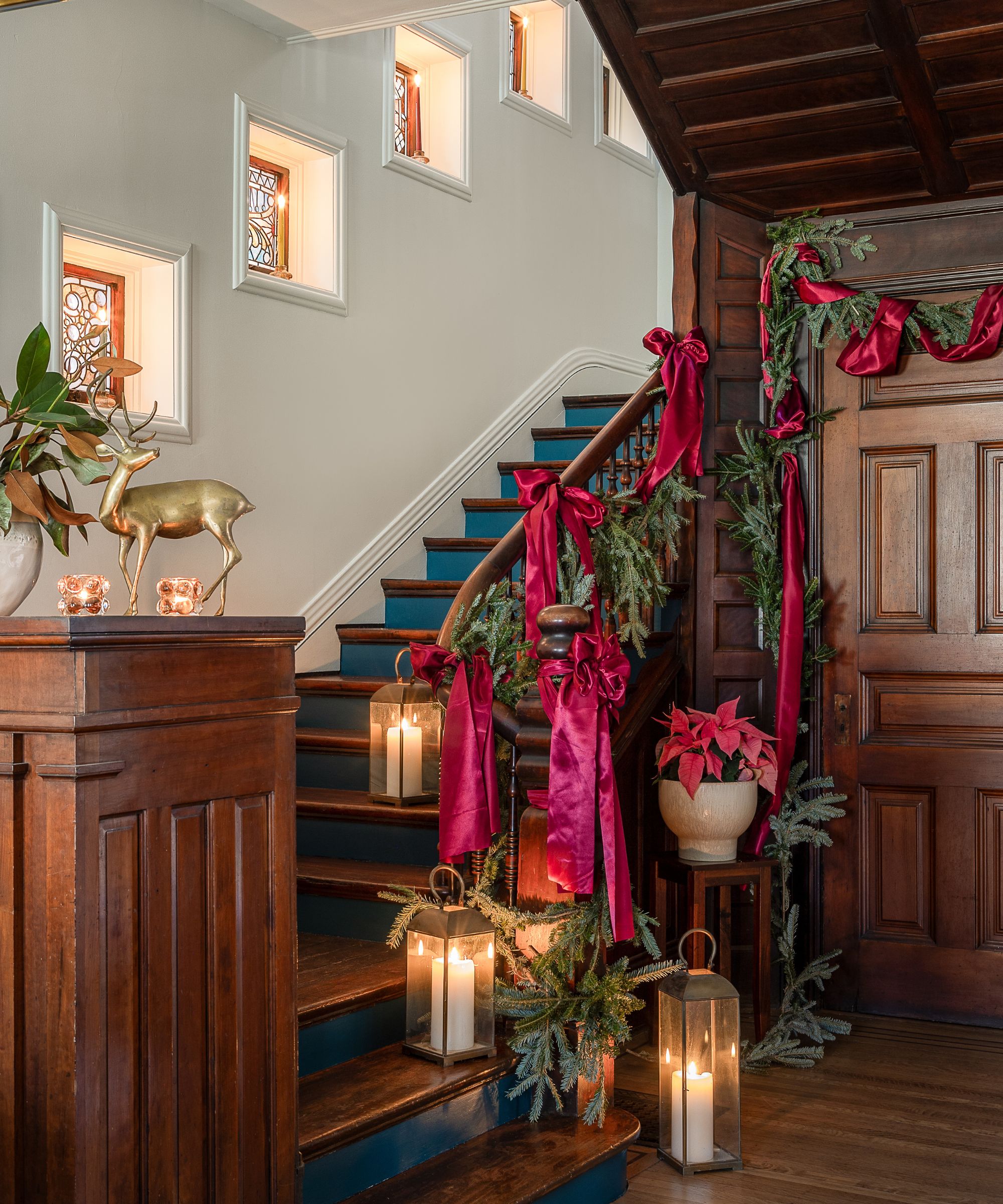 entrée en bois sombre avec des escaliers historiques en bois sombre décorés pour Noël avec des guirlandes, des nœuds en satin et des lanternes