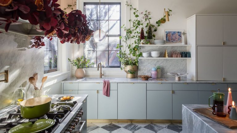 Comment la créatrice Bethany Adams réinvente un Noël classique avec des couleurs vives et un charme nostalgique a pale blue modern kitchen in a historic home with checkerboard floor decorated for christmas with a red foliage and orange garland over the stove and little bottle brush trees and candles