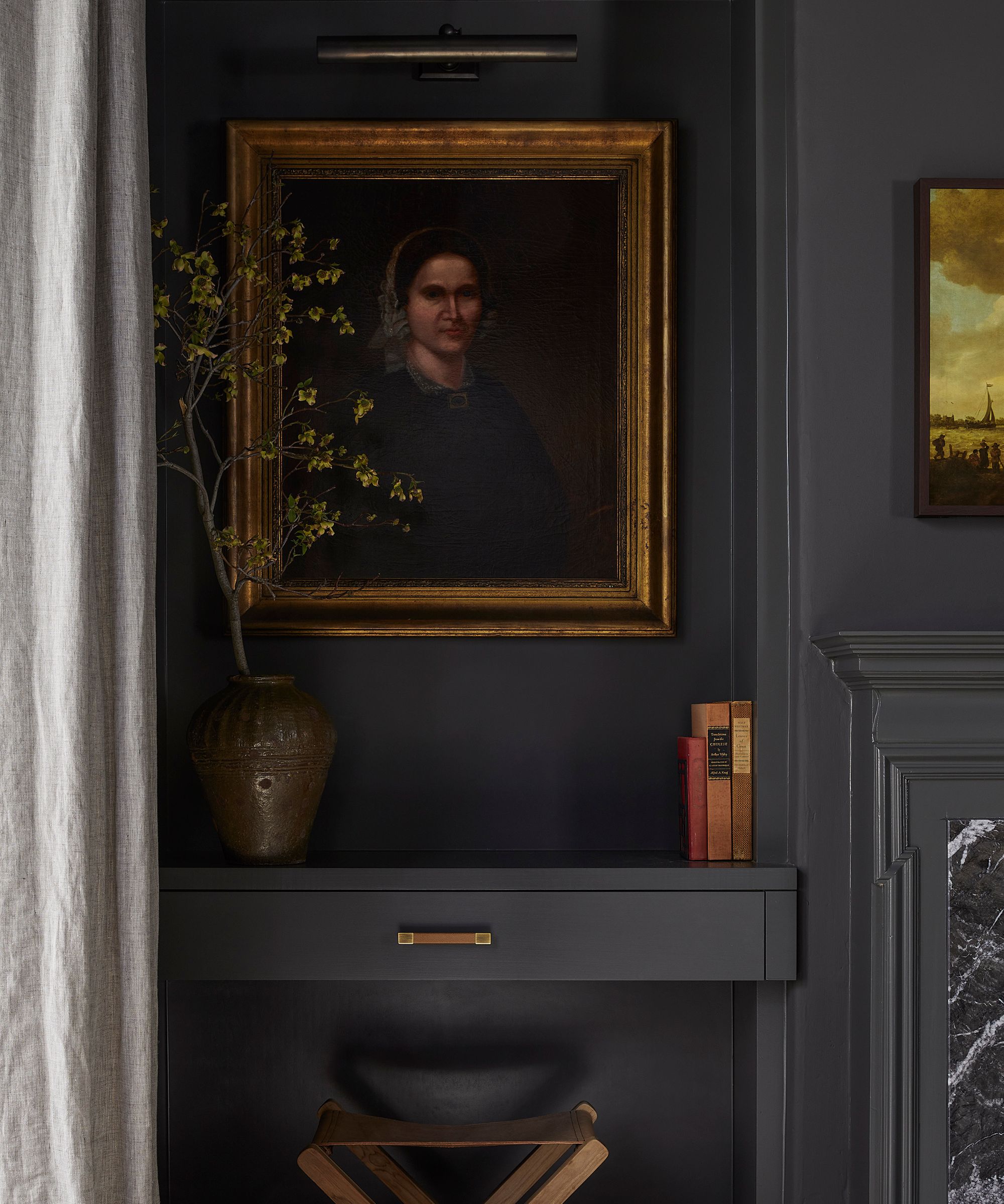 Gros plan d'un mur gris foncé avec un portrait classique dans un cadre doré éclairé par une lumière artistique, au-dessus d'un bureau/étagère flottant