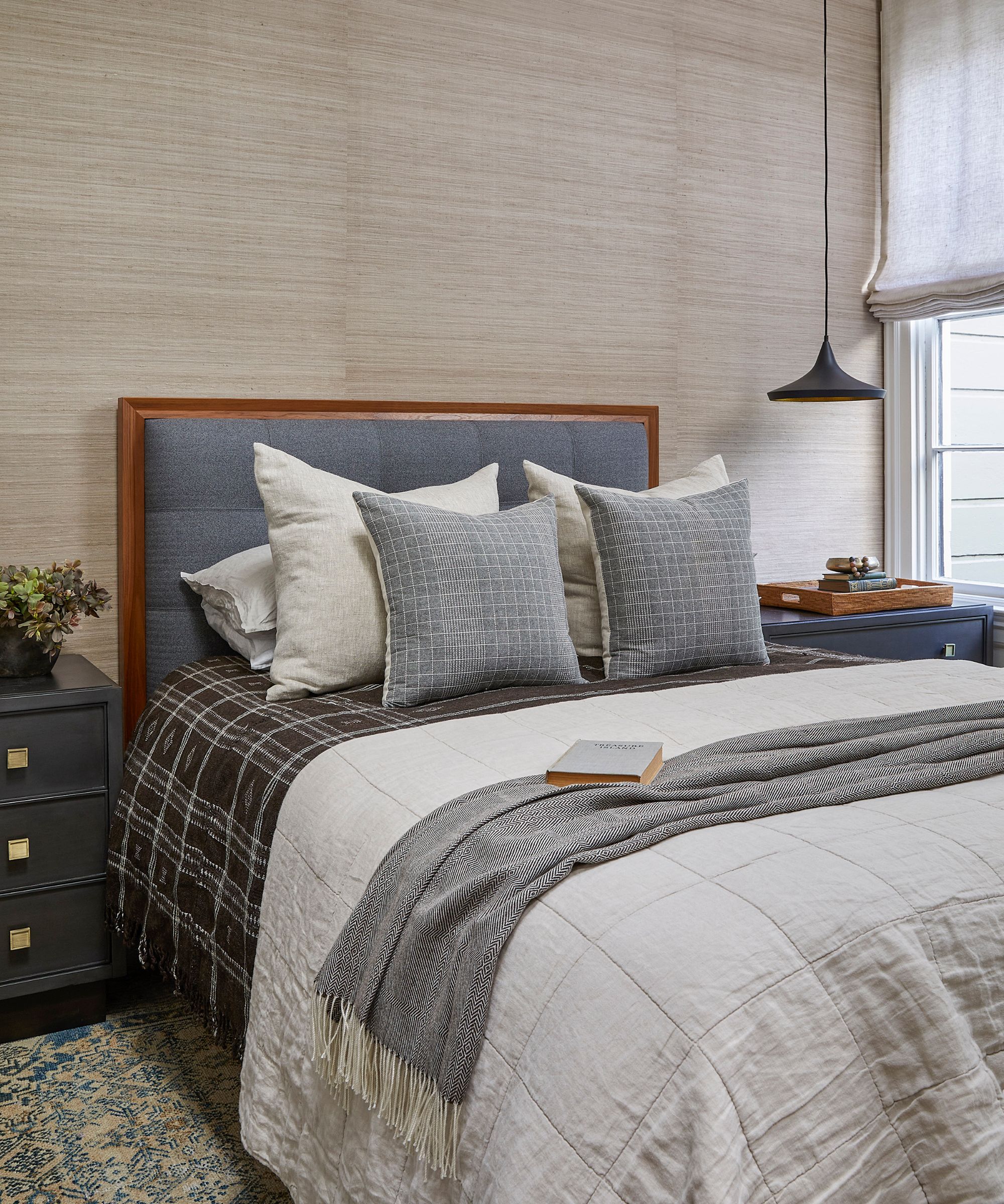 Chambre neutre avec papier peint en toile de jute, tête de lit rembourrée grise et tables de nuit gris foncé avec quincaillerie en laiton