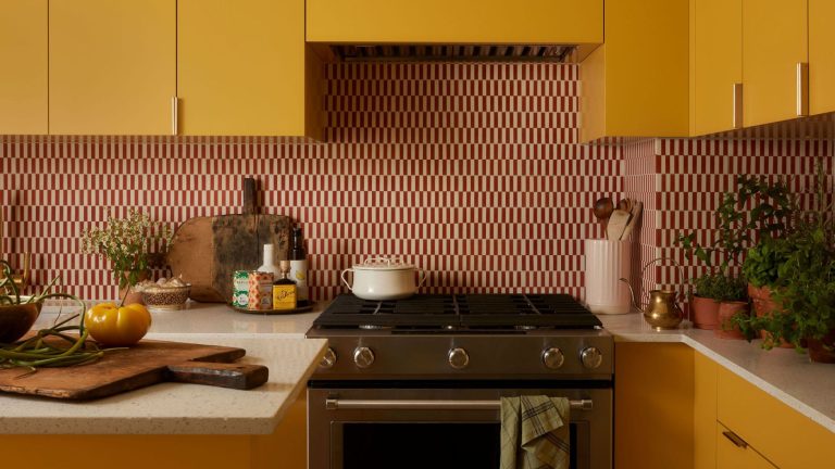 Comment un petit condo de 750 pieds carrés à Toronto, avec une seule fenêtre, a été entièrement retravaillé avec de nouveaux aménagements, des couleurs vives et un rangement astucieux Close-up of a sunny yellow kitchen counter with a stove, a toaster, potted herbs, and an open cabinet revealing dishes and bottles