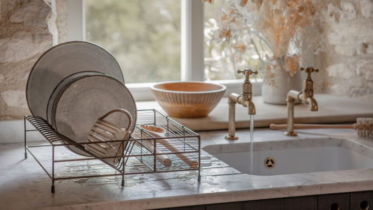 Les propriétaires sont invités à trouver et à étiqueter cette vanne cruciale dès maintenant – avoir du mal à la trouver en cas de fuite pourrait signifier 1 000 $ de plus en réparations A metal plate drying rack next to sink set into a stone kitchen counter top.