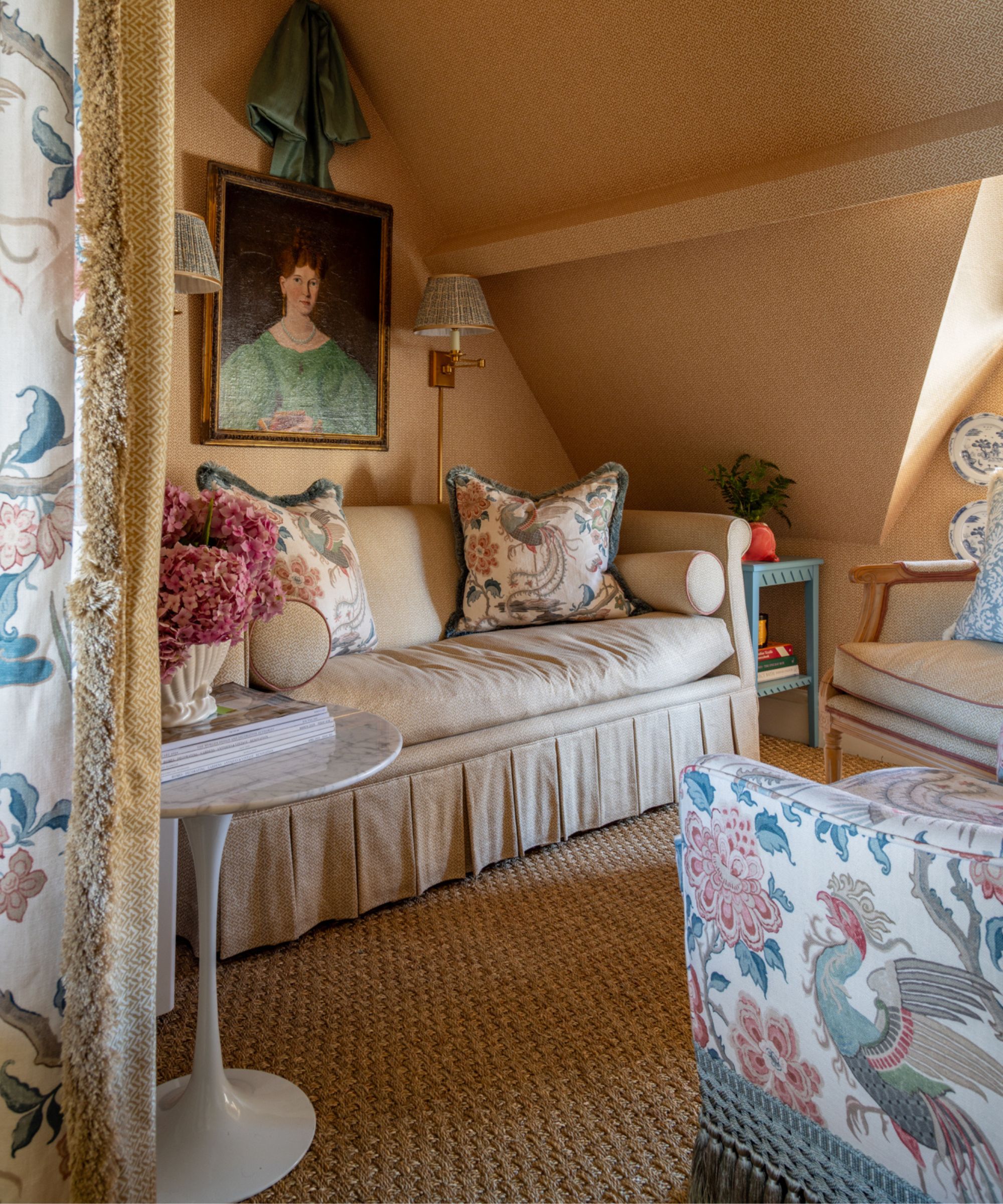 coin salon recouvert de papier peint jaune chaud avec un canapé à jupe orné d'oreillers à motifs à franges assis en face d'un fauteuil à fleurs avec bordure à pampilles