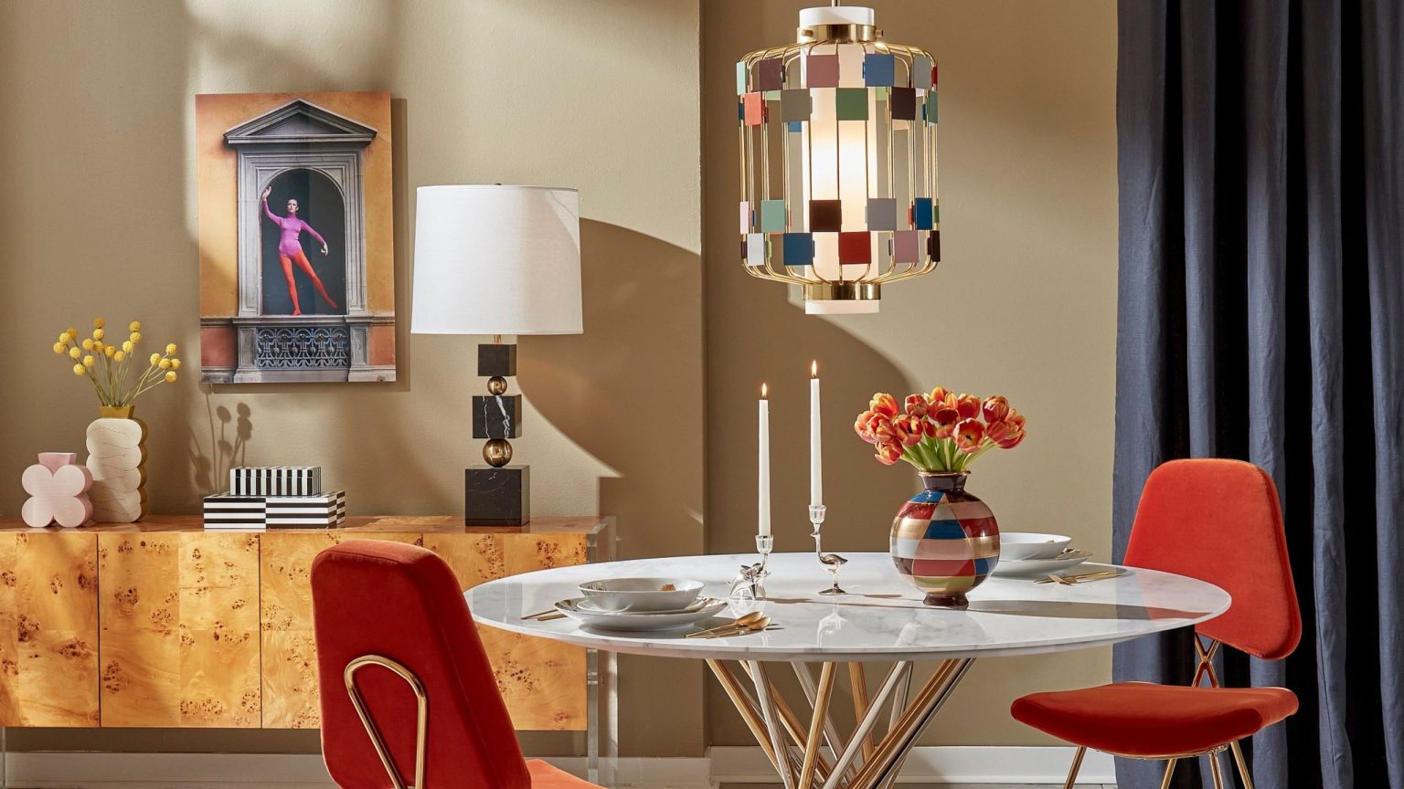 Playful Jonathan Adler-designed living room featuring colorful geometric Deco-inspired lighting and vases, jewel-toned velvet dining chairs, a circular marble dining table, and a burlwood sideboard.