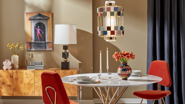 Playful Jonathan Adler-designed living room featuring colorful geometric Deco-inspired lighting and vases, jewel-toned velvet dining chairs, a circular marble dining table, and a burlwood sideboard.