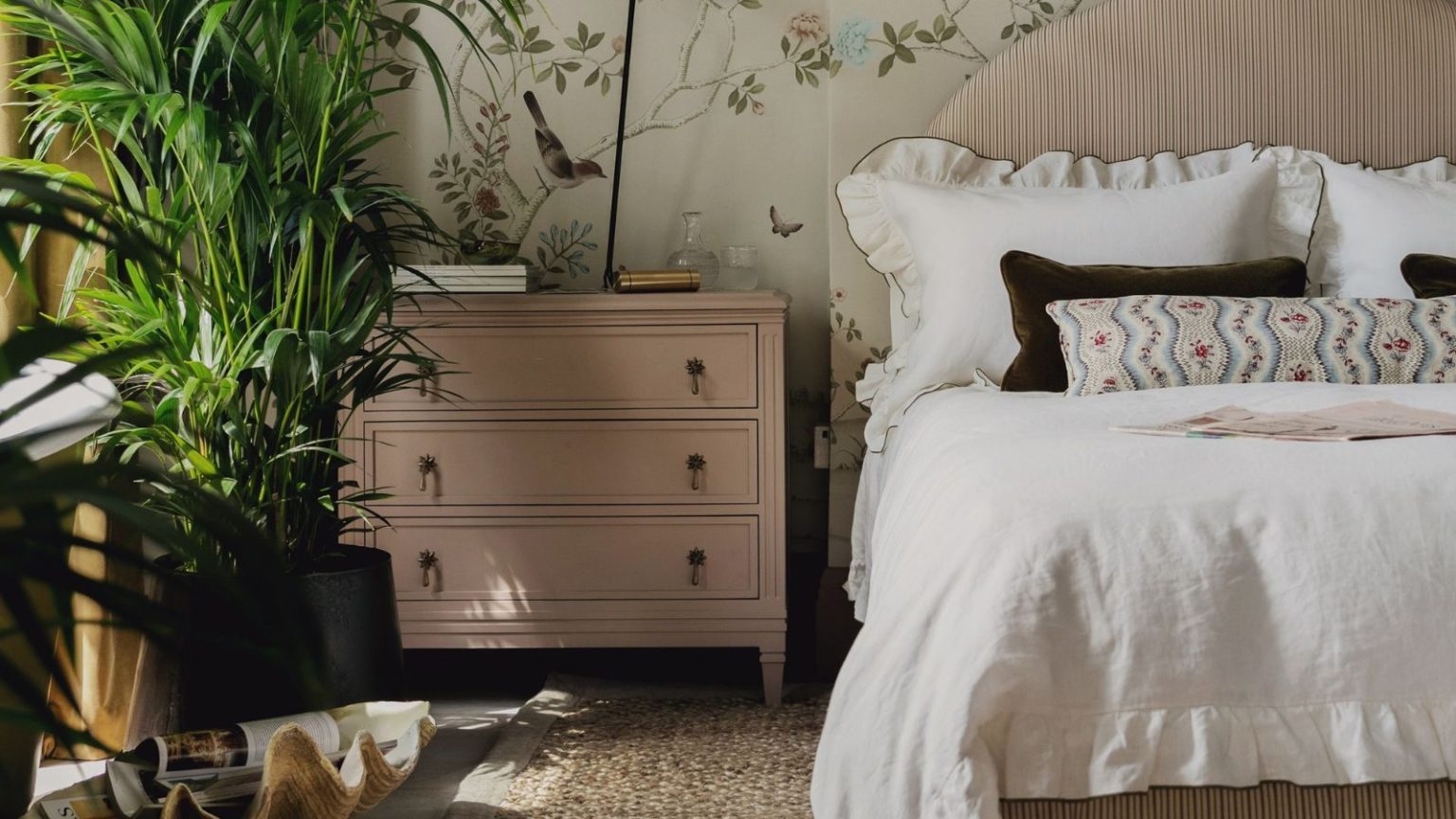 5 tendances en matière de literie que seuls les designers utilisent actuellement – et comment acheter le look de chambre de luxe romantic pale pink bedroom with floral mural wallpaper, a pink striped headboard, white ruffle trim bed linen and large indoor plants