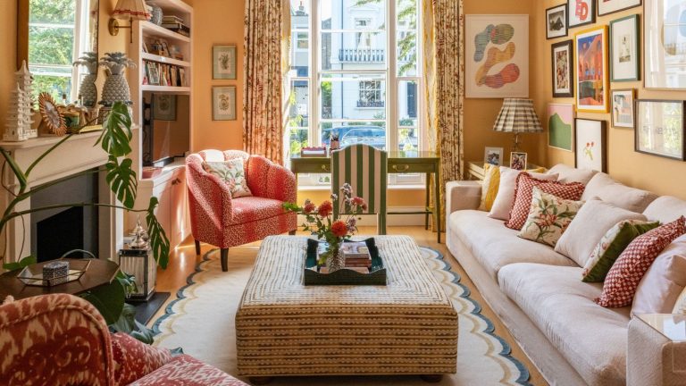 warm yellow orange living room traditional English style with a fireplace, large cream couch, gallery wall, a scalloped rug and an upholstered ottoman