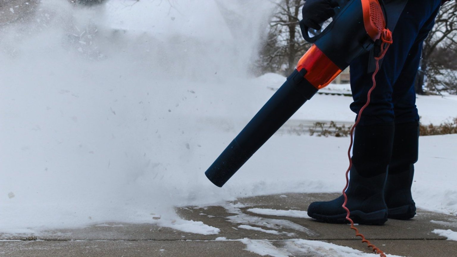 Avez-vous déjà eu envie d’utiliser une souffleuse à feuilles pour la neige ? Les experts révèlent quand vous pouvez et ne pouvez pas, et comment le faire efficacement A person is using a corded leaf blower to blow snow from their driveway