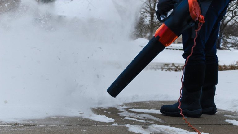 Avez-vous déjà eu envie d’utiliser une souffleuse à feuilles pour la neige ? Les experts révèlent quand vous pouvez et ne pouvez pas, et comment le faire efficacement A person is using a corded leaf blower to blow snow from their driveway
