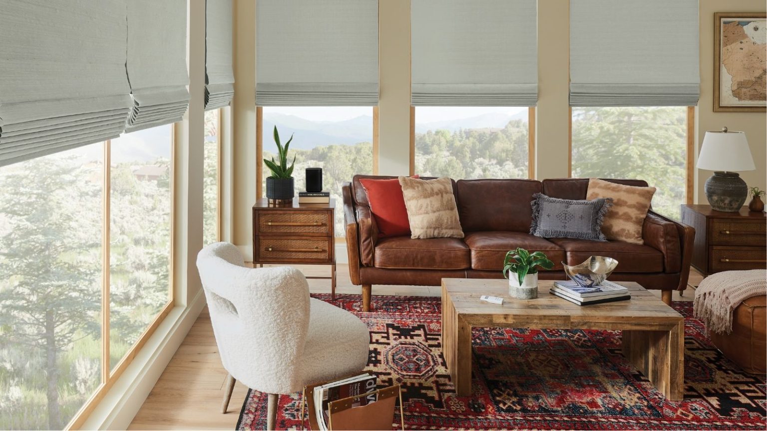 Cette astuce CVC simple a résolu instantanément les radiateurs à chauffage lent et les points froids dans ma maison Small living room with windows revealing trees and green space outside, partially covered by gray blinds. Pictured in the living room are a brown sofa, a white armchair, wooden drawers and coffee table, and a red patterned rug.
