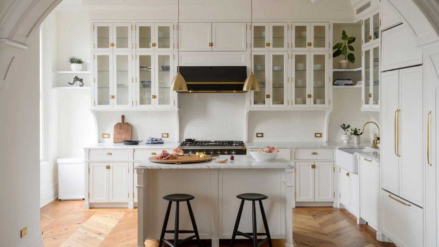 Ces 3 tendances d’armoires exagérées donneront du goût à votre cuisine en 2026 Fitted white country kitchen through period archway with kitchen island and brass fittings on parquet floor
