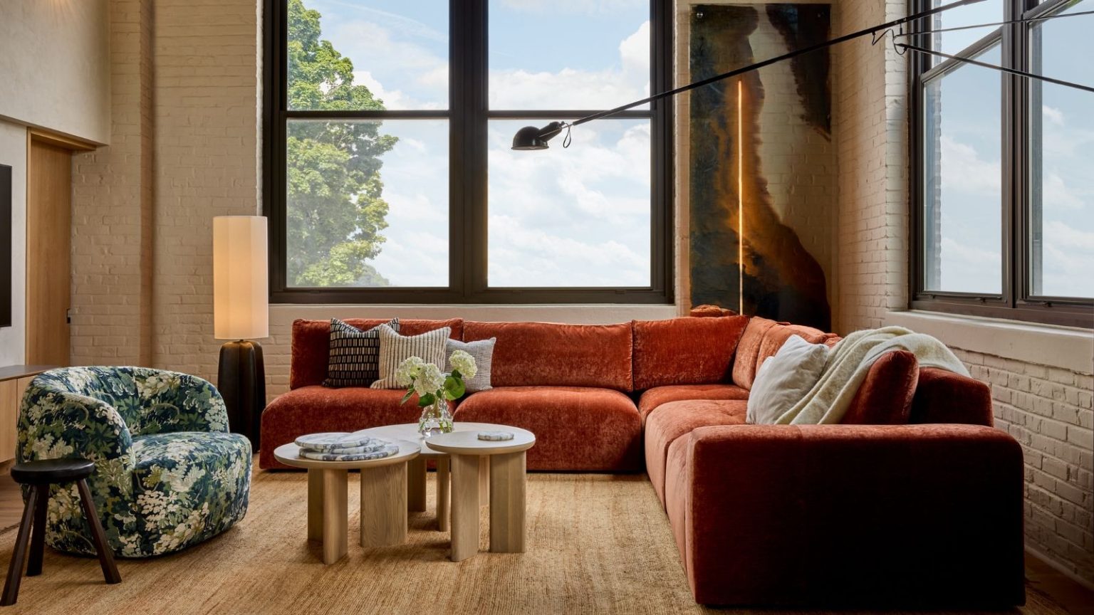 Si votre famille continue de rembobiner les films de Noël parce que le son est mauvais, ce système Samsung à 200 $ de réduction le résout Colorful living room with orange velvet sofa, green patterned armchair, modular coffee table, and large, bright windows. Exposed brick walls and modern lighting are pictured around the furniture.