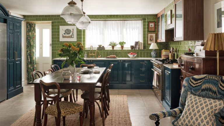A green tiled kitchen with blue cabinetry and a dark oak table in the centre.