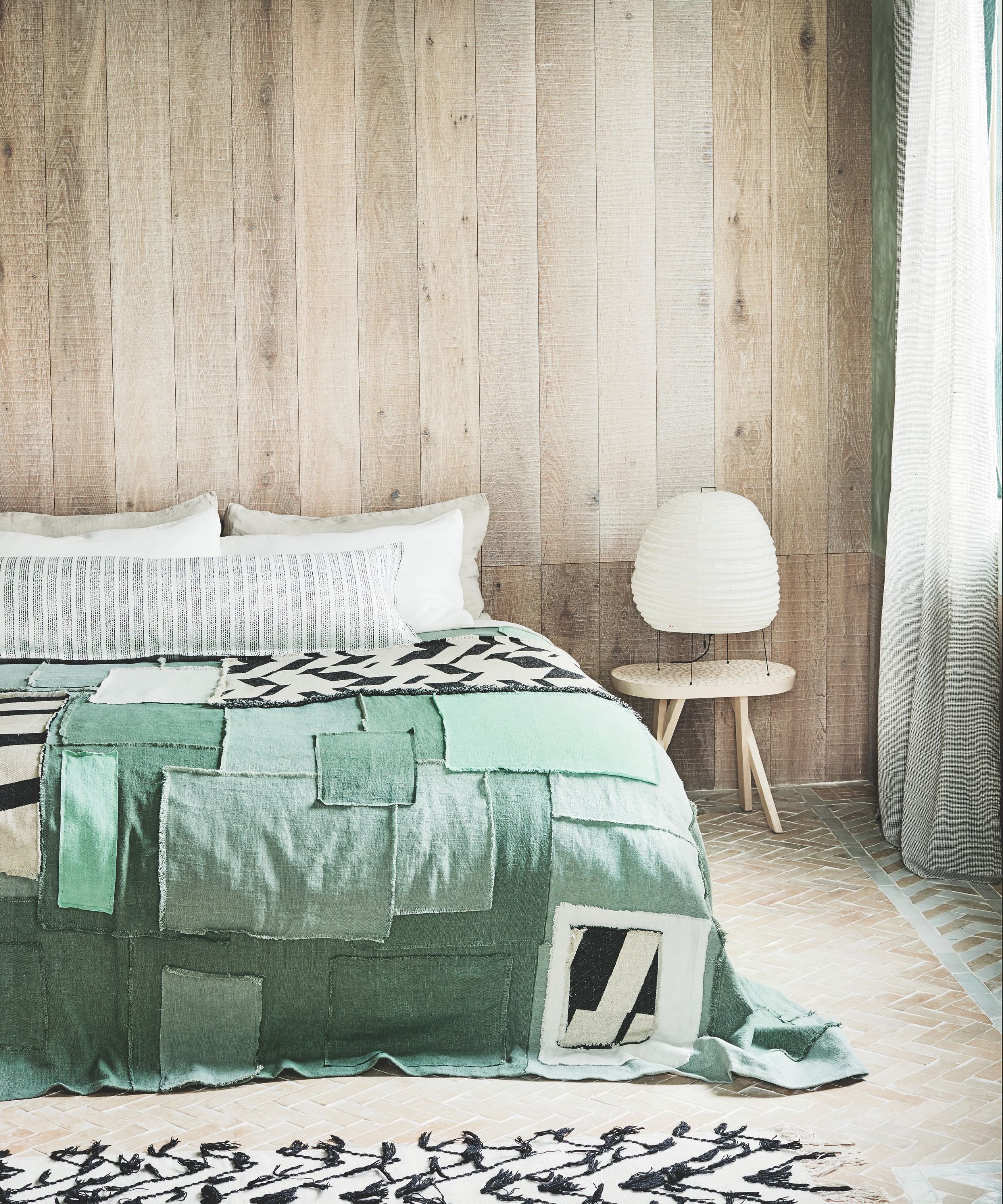 Chambre avec mur revêtu de bois, lit double avec couvre-lit en patchwork vert, parquet et tapis noir et blanc.