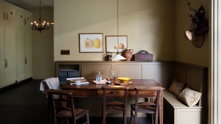 Light taupe dining corner with built in L-shaped benches in dark taupe paint, mid-century wooden table with four dining chairs, and built-in floor-to-ceiling cabinetry on the left